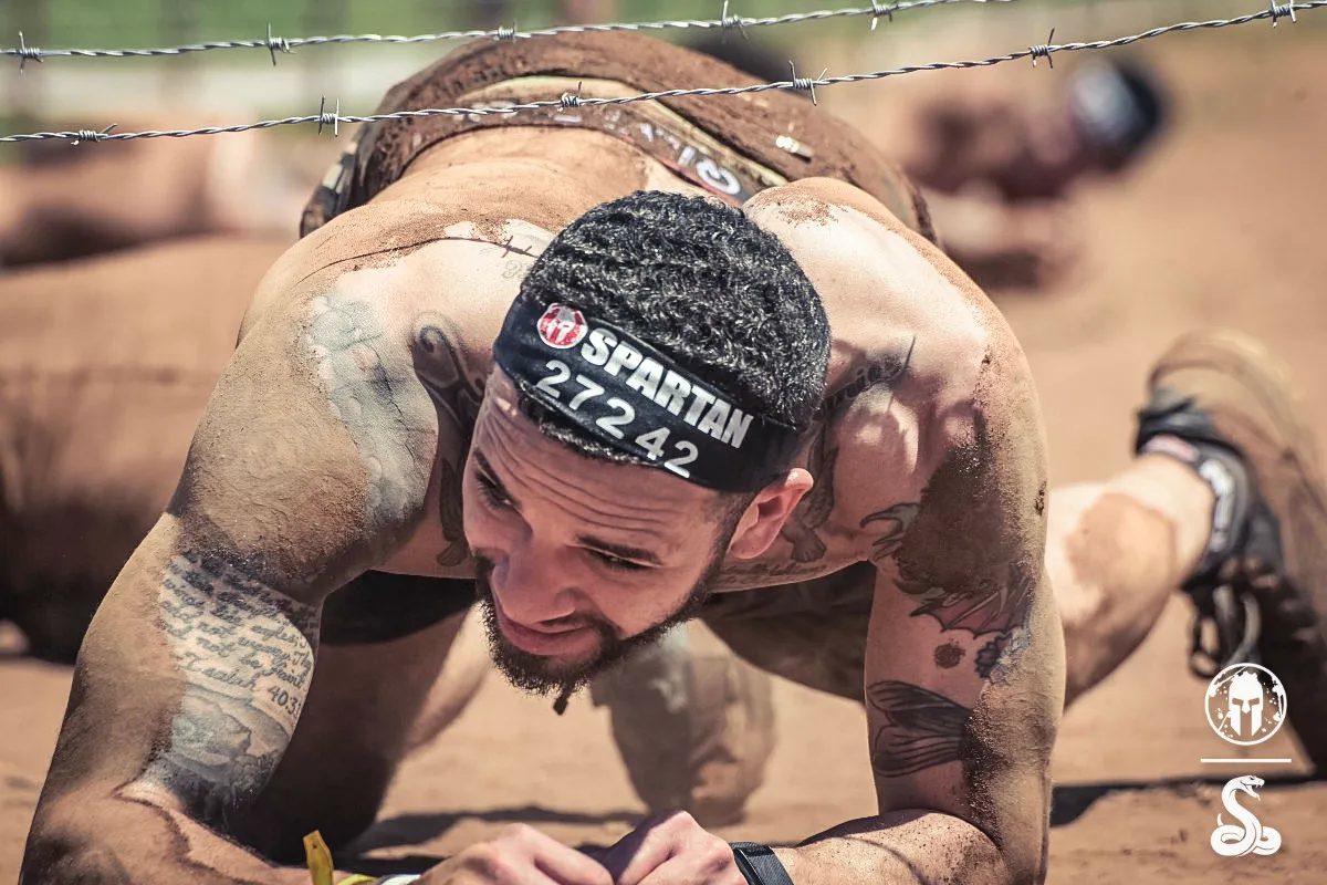 Cameron crawling under barbed wire at a Spartan race, covered in dirt
